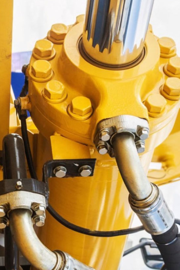 Close-up of a yellow hydraulic cylinder with a chrome piston rod, bolts, and hoses connected to it.