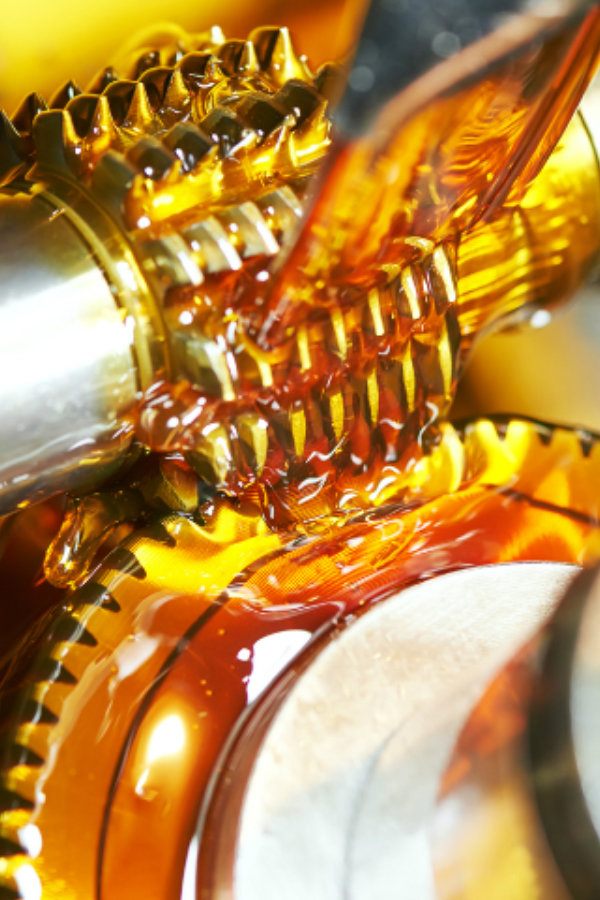 Close-up of interlocking metal gears coated in golden oil inside a gearbox. in operation inside industrial machinery
