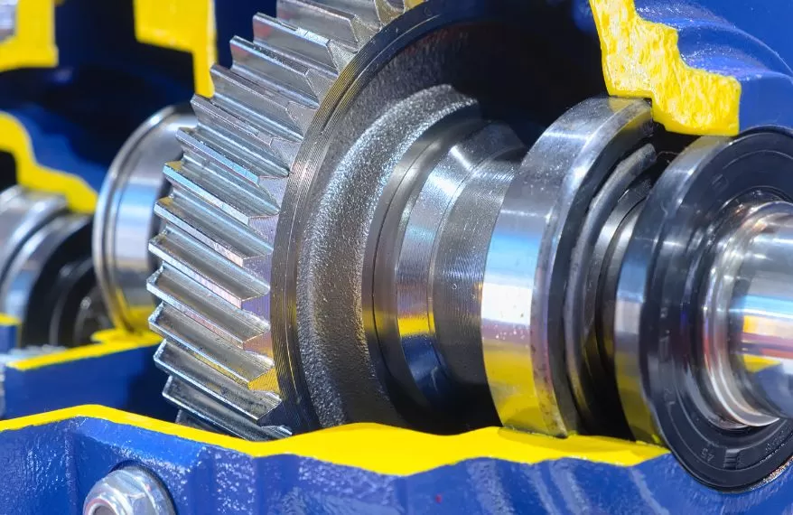 Close-up of a metallic gear inside a blue and yellow gearbox housing during machining or assembly.