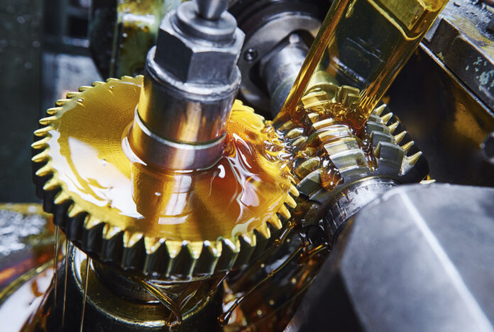 Close-up of interlocking metal gears coated in golden oil inside a gearbox. in operation inside industrial machinery