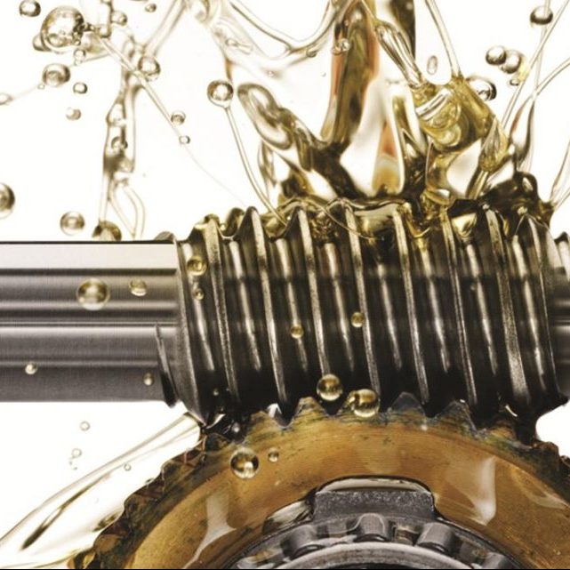 Close-up of a metal threaded shaft and gear with splashing lubricant or oil around them.